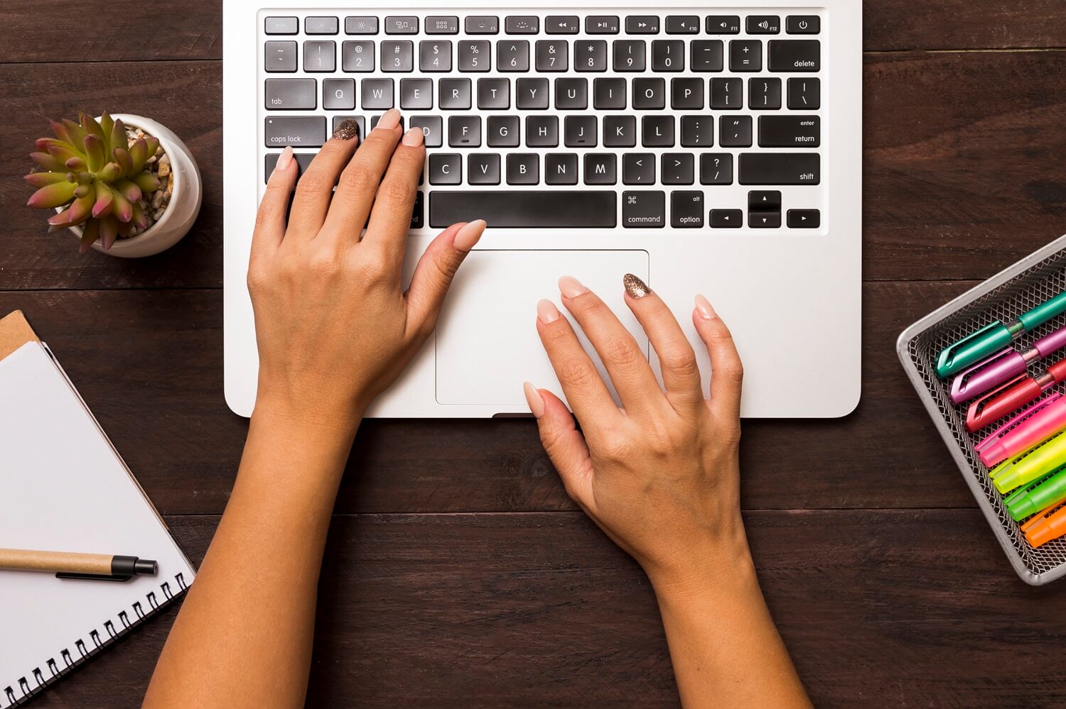 Personne tapant au clavier d'un ordinateur avec des feutres colorés posés sur son bureau